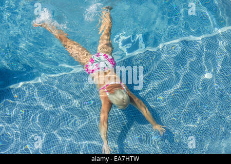 High angle view of aged woman that is swimming underwater in bright blue water of pool. Stock Photo