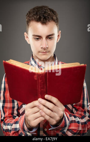Handsome teenage boy reading an old book, over gray background Stock Photo