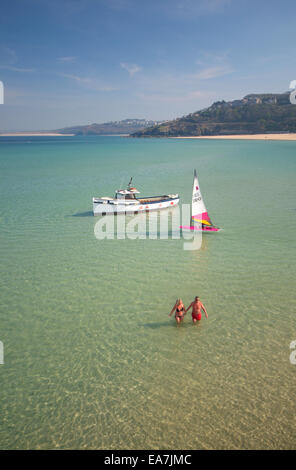 Looking down at couple in swimware hand in hand paddling in crystal clear water with boat at anchor & yacht St Ives Bay Penwith Stock Photo