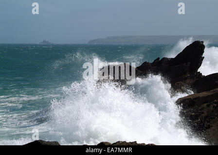 Waves crashing onto rocks St Ives Bay with Godrevy Lighthouse & Island in distance Penwith West Cornwall South West England UK Stock Photo