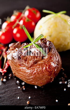 Piece of red meat steak with rosemary served on black stone surface. Stock Photo