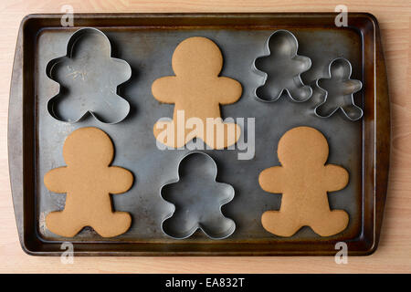 High angle shot of an old baking sheet with Christmas gingerbread man cookies and cookie cutters. Horizontal format on wood kitc Stock Photo