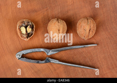 High angle shot of three walnuts and a nutcracker on a wood surface, one nut is cracked in half. Horizontal format. Stock Photo