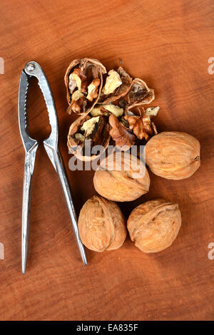 High angle shot of some walnuts and a nutcracker on a wood surface, one nut is cracked in half. Vertical format. Stock Photo