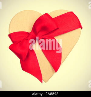 a heart-shaped gift box with a red ribbon on a beige background, with a retro effect Stock Photo