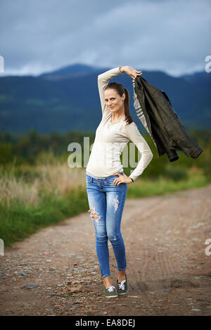 Young caucasian woman outdoor on a rural dirt road in the countryside with mountains behind her Stock Photo