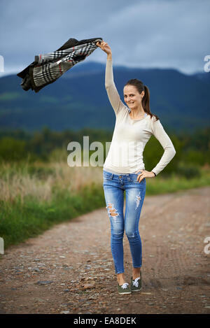 Young caucasian woman outdoor on a rural dirt road in the countryside with mountains behind her Stock Photo