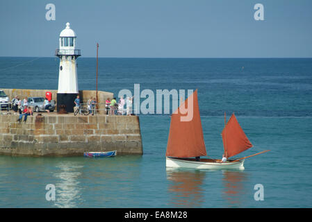 White hulled brown sailed Lugger sailing into St Ives Harbour past Smeatons pier & lighthouse on a calm hazy summers afternoon P Stock Photo