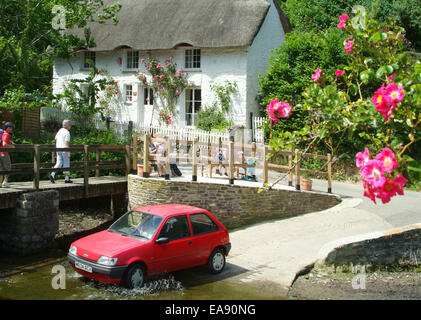 Red car driving across a ford in the pretty village of Helford on the Lizard Peninsula Kerrier South West Cornwall South West En Stock Photo