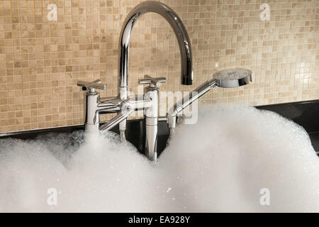 bathtub full of foam with chrome faucet on a background of mosaic tiles Stock Photo