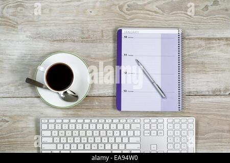 Top view of business office objects consisting of calendar, pen, computer keyboard and cup of coffee on white wooden desktop Stock Photo