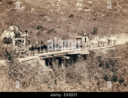 The Deadwood Coach - Two stagecoaches crossing a bridge; men in wagons are waving or tipping their hats to the photographer. 1889 Stock Photo
