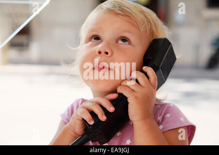 Outdoor portrait of surprised little Caucasian blond girl talking on the street phone Stock Photo