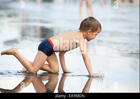 Little boy crawls  in puddle Stock Photo