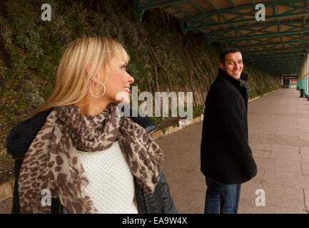 A man and woman out walking both look back over their shoulders and smile Stock Photo