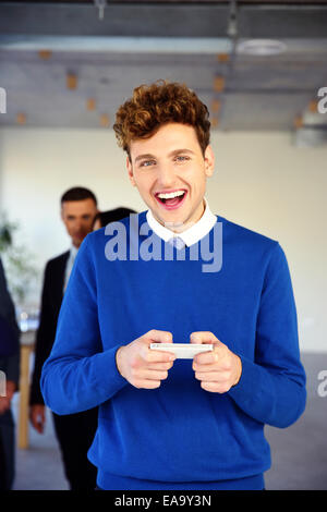 Laughing young businessman standing with smartphone in office Stock Photo
