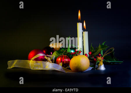 A Christmas still-life including lit candles, baubles,ribbon,fruit and holly with berries Stock Photo