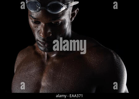 Young african male swimmer looking down in thought. Close-up image of pensive young man with swimming goggles and wet body. Stock Photo