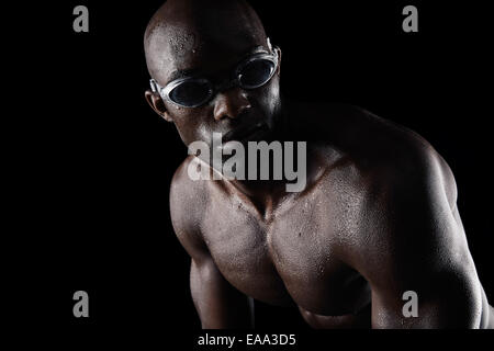 African male athlete with swimming goggles looking away on black background. Professional swimmer practicing. Stock Photo
