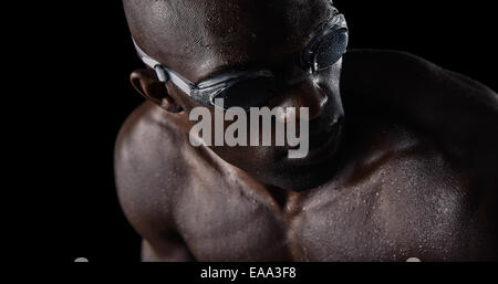 Close-up image of African male athlete with swimming goggles looking over shoulder. Professional swimmer on black background. Stock Photo