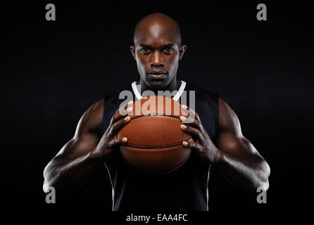Portrait of afro american male basketball player with a ball over black background. Fit young man in sportswear holding ball.