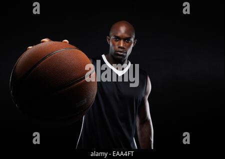 Image of young man holding a basketball against black background with copy space. Fit basketball player with focus on ball. Stock Photo