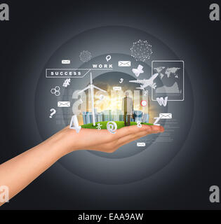 Hand holds city of skyscrapers on green grass and businessman walking forward. Flying letters near hand Stock Photo