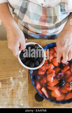 Woman pouring stewed fruit into a pie dish. Fresh blackberries. Stock Photo