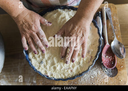 Woman patting crumble mixture into a pie dish, making a fruit crumble pudding. Stock Photo