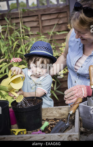 A woman and a young child water new seeds planted in a pot. Stock Photo
