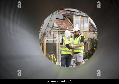 Two construction workers at a building site, viewed through a round pipe. Stock Photo