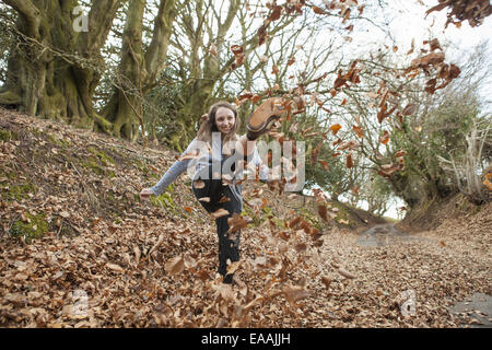 Young woman playing in fallen leaves, kicking them in the air. Stock Photo