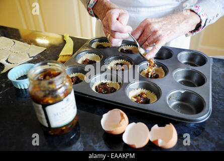 Elderly woman pensioner baking mince pies at home in her kitchen for Christmas . Putting the mincemeat into the pastry shells Stock Photo