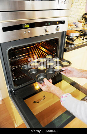 Elderly woman pensioner baking mince pies at home in her kitchen for Christmas . Putting them into the oven Stock Photo