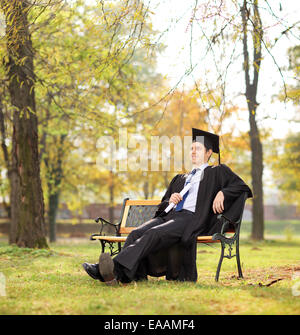 Graduate student holding diploma seated on bench in park shot with tilt and shift lens Stock Photo