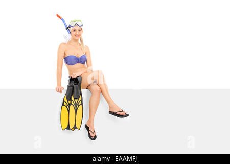 Woman in bikini holding flippers seated on a panel isolated on white background Stock Photo