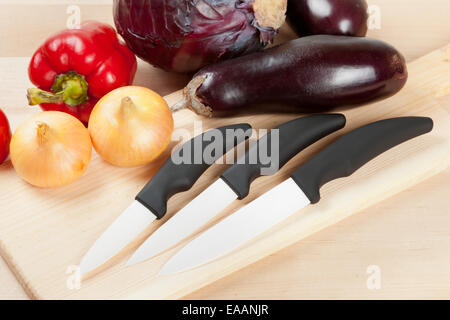 ceramic knifes with vegetables on cutting board Stock Photo