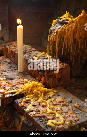 Vertical close up of a lit votive candle and layers of old melted wax in Pak Ou or Tam Ting caves Stock Photo