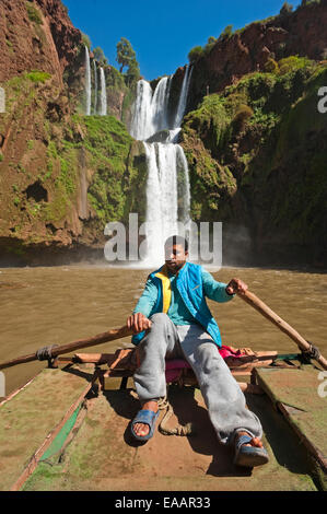Vertical portrait of a young Moroccan man rowing a tour boat at the bottom of Cascades d'Ouzoud on a sunny day. Stock Photo