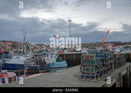 Lobster and crab pots on the quayside with fishing boats in Whitby, North Yorkshire, England, UK Stock Photo