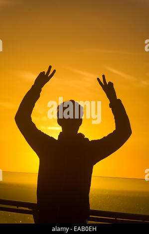 Silhouette of a man at sunrise giving the peace / victory hand sign ...
