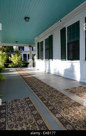 a large outdoor front porch.  The floor is wood which is painted and has been covered with carpets.  The exterior of the house i Stock Photo