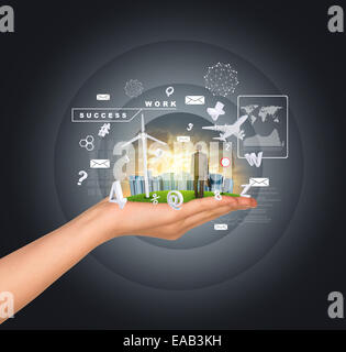 Hand holds city of skyscrapers on green grass and businessman walking forward. Flying letters near hand Stock Photo