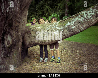 Boy and girl hide behind tree branch Stock Photo