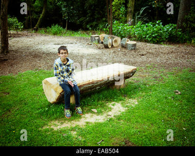 Boy sits on sawn log bench in park Stock Photo