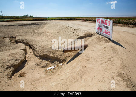 A farmers sign about the water crisis next to a farmers dried up waterhole, folllowing a 4 year long drought, near Bakersfield in the Central Valley, California, USA, with the soil turned to dust. The whole of California is in a catastrophic drought with $2.2 Billion annually lost from the agricultural sector, with many workers laid off. One third of children in California currently go to bed hungry. 428,000 acres of farmland have been taken out of production in the Central Valley due to the drought. Stock Photo
