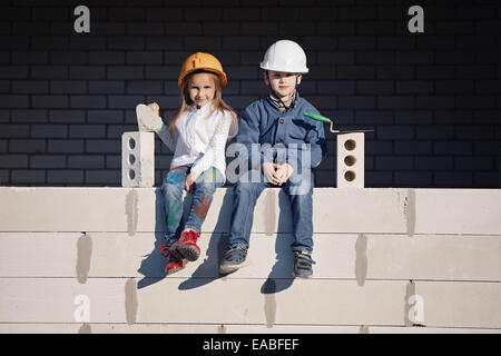 little boy and girl in helmets build house Stock Photo