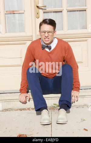 angry  handsome man with glasses and sweater sitting on steps in front of house and posing  while looking at camera, vintage ret Stock Photo