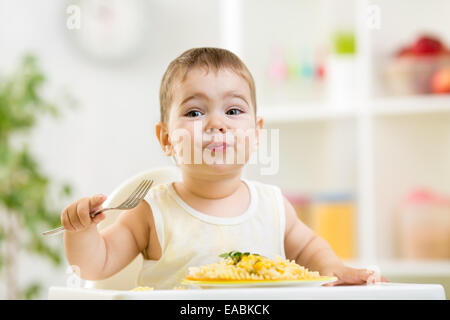 cute kid boy in a highchair for feeding with a fork and a pasta Stock Photo