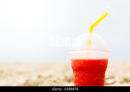 Red fruit icy cocktail in beach sand. Traveling and relaxing concept. Space for your text. Stock Photo